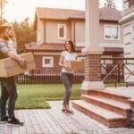 A young couple smiles as they unpack a moving box in their new, sunlit living room, representing a successful and happy spring move in Edmonton.