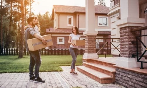 A young couple smiles as they unpack a moving box in their new, sunlit living room, representing a successful and happy spring move in Edmonton.