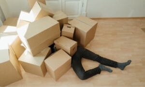 An individual overwhelmed by the moving process, peeking out from under a mountain of stacked boxes.