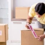 A professional mover from Stallion Vanlines carefully wrapping a large, framed piece of art in protective glassine paper before placing it in a custom moving crate.