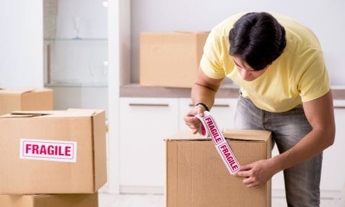 A professional mover from Stallion Vanlines carefully wrapping a large, framed piece of art in protective glassine paper before placing it in a custom moving crate.