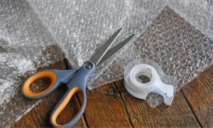 A close-up of essential specialty moving supplies, including a wooden crate, high-quality bubble wrap, corner protectors, and heavy-duty moving blankets.